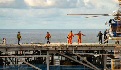 Crew members board and monitor a helicopter on a helideck offshore