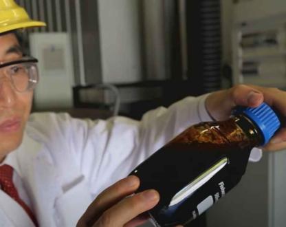 Man in hard hat holding a glass bottle full of dark brown liquid