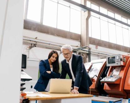 Two professional looking at a laptop in a manufacturing facility.