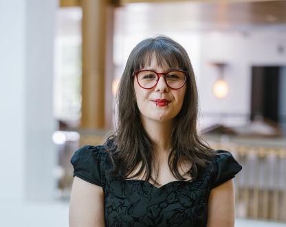 Photo of Kiowa Scott-Hurley holding a walking stick and standing in the foyer of an office building