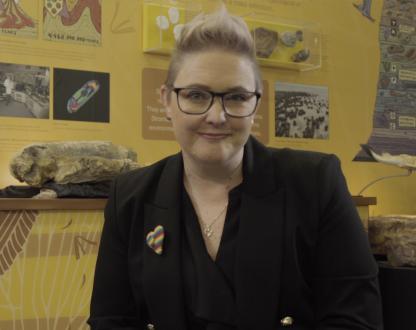 Dr Verity Normington stands in front of a display of several different types of rock
