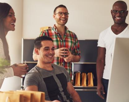 A group 4 people in an office looking at a computer screen, smiling.