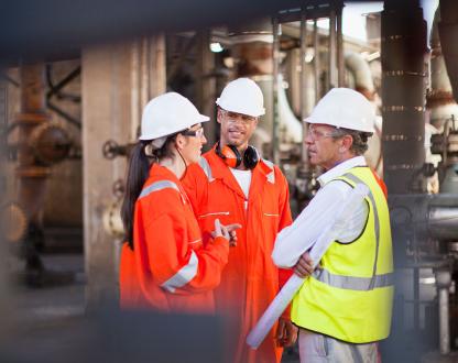 Three people wearing protective clothing meet on an offshore oil and gas facility