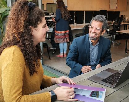 A businessman and women have a conversation at a table over a laptop. 