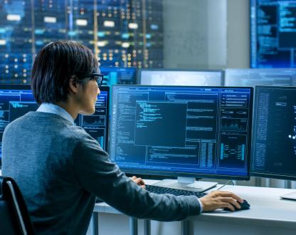 Person sitting at a desk with three computer monitors in front of them displaying artificial intelligence-related data. 