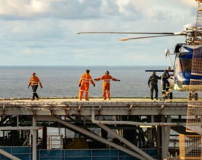 Crew members board and monitor a helicopter on a helideck offshore