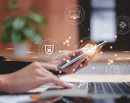 Photo of a person on their laptop holding a mobile phone. Superimposed with icons representing different technologies.