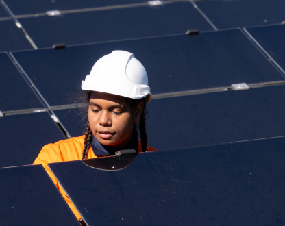 Female Aboriginal Australian technician inspecting photovoltaic panels on solar farm wearing hi-vis workwear