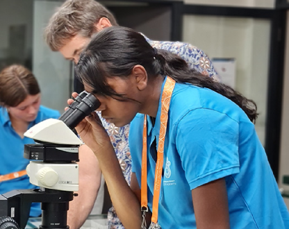 Female student looking into a microscope while a teacher looks on.