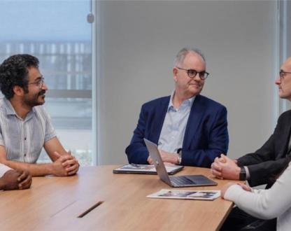 A still from the George Medicines Brandon Capital video showing people sitting around a table talking. 