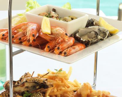 Cooked prawns and fresh oysters arranged on a white platter, served with lemon wedges.