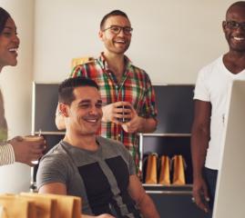 A group 4 people in an office looking at a computer screen, smiling.