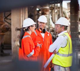 Three people wearing protective clothing meet on an offshore oil and gas facility