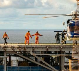 Crew members board and monitor a helicopter on a helideck offshore