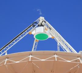 A green circular Phased Array Feed receiver, housed in white casing designed by Innovation Composites, sits on top of an ASKAP telescope dish pointing to the sky