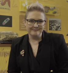 Dr Verity Normington stands in front of a display of several different types of rock